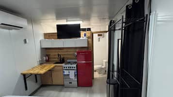 A compact room with a bed, a kitchenette with a stove, a refrigerator, and a small window.