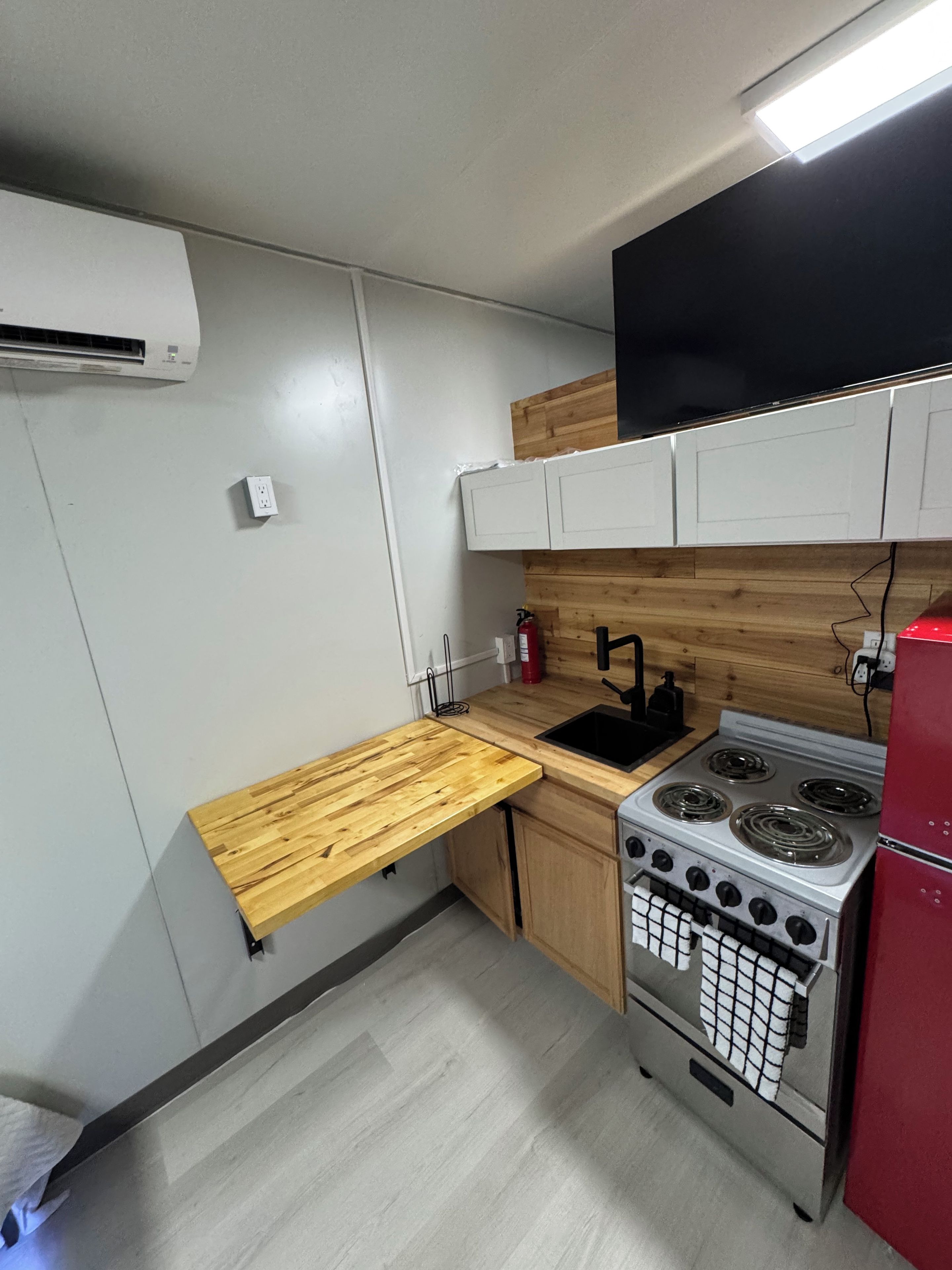 A compact kitchen with a wooden countertop, a stove, a sink, and a red refrigerator.