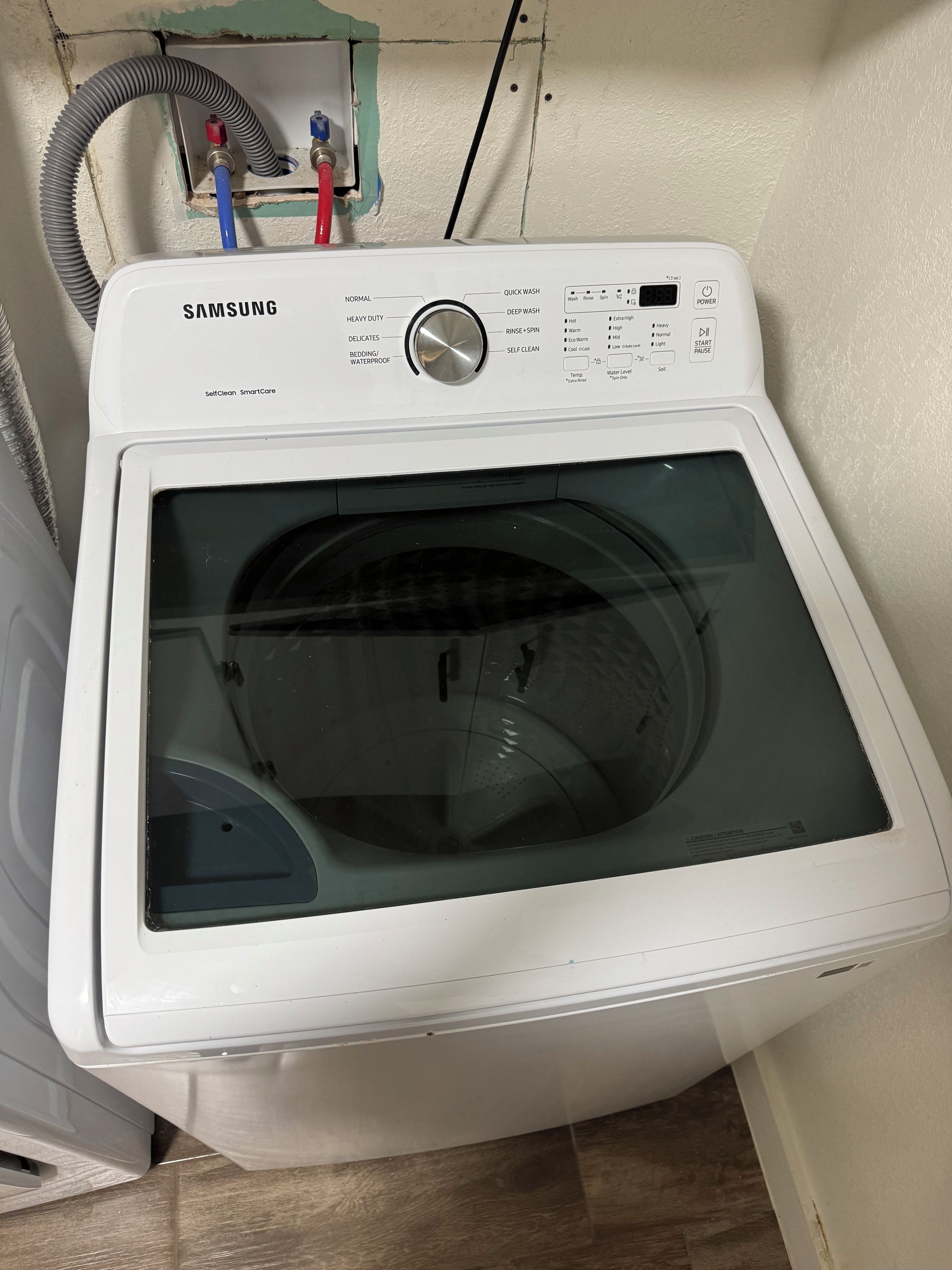 Una lavadora Samsung SmartCare de limpieza automática con panel de control, puerta transparente y conexión para manguera.