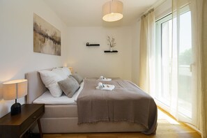 A bedroom with a bed, bedside table, lamp, artwork, and a window with curtains. - Luxury 4-room Apt in Japandi-style I Prime Location I Family-friendly I Balcony I Kitchen I Netflix I Free Parking I 105 m2 (Eltville am Rhein)