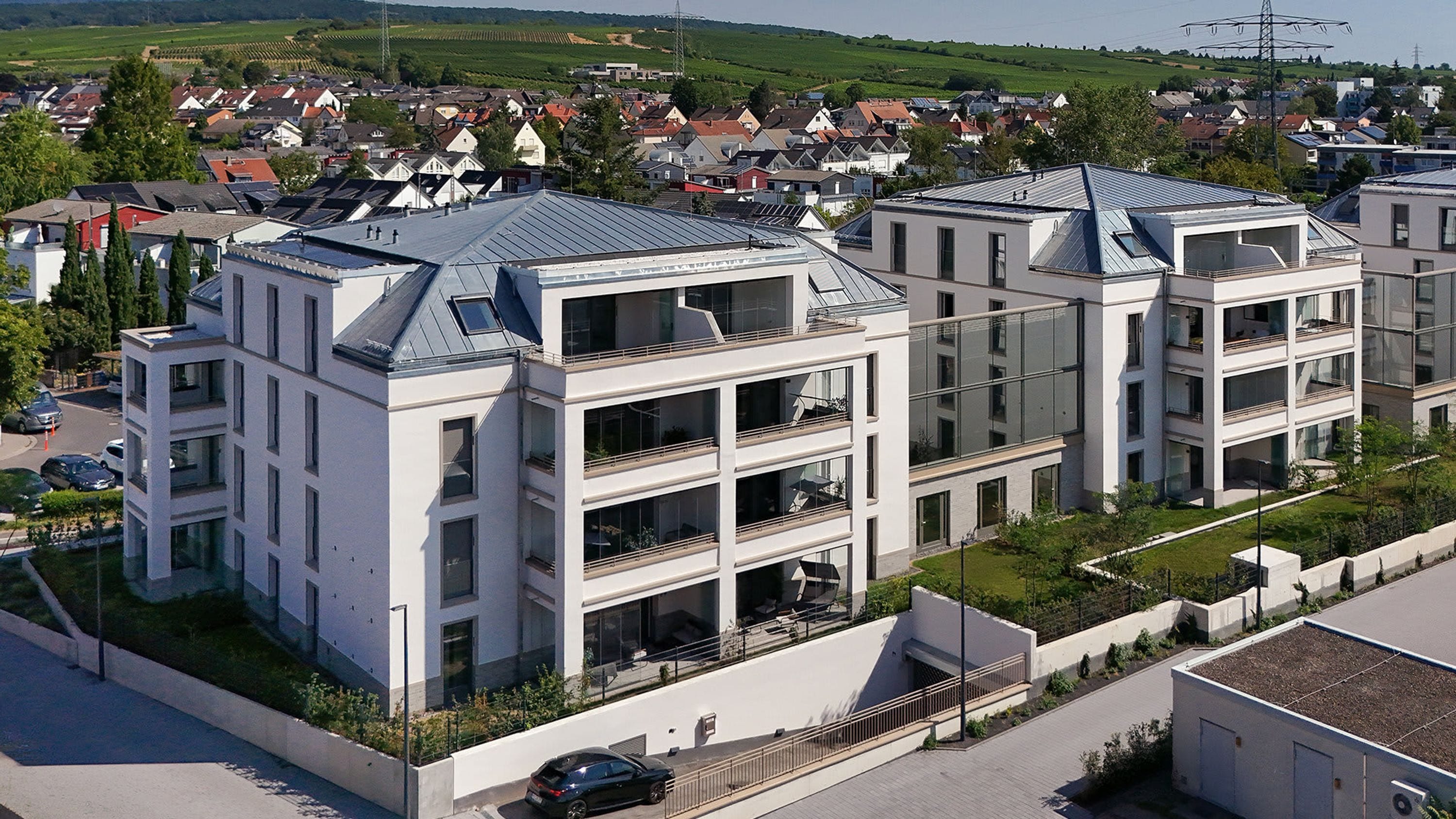 Un moderno edificio residencial de varios pisos con balcones, techo plano y un paisaje verde circundante.