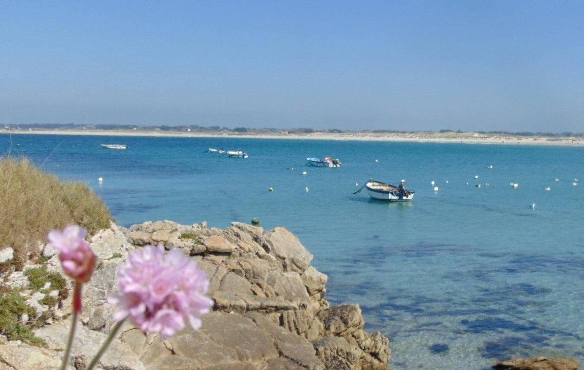Un paysage côtier avec des bateaux sur une eau calme, une côte rocheuse et un ciel dégagé.