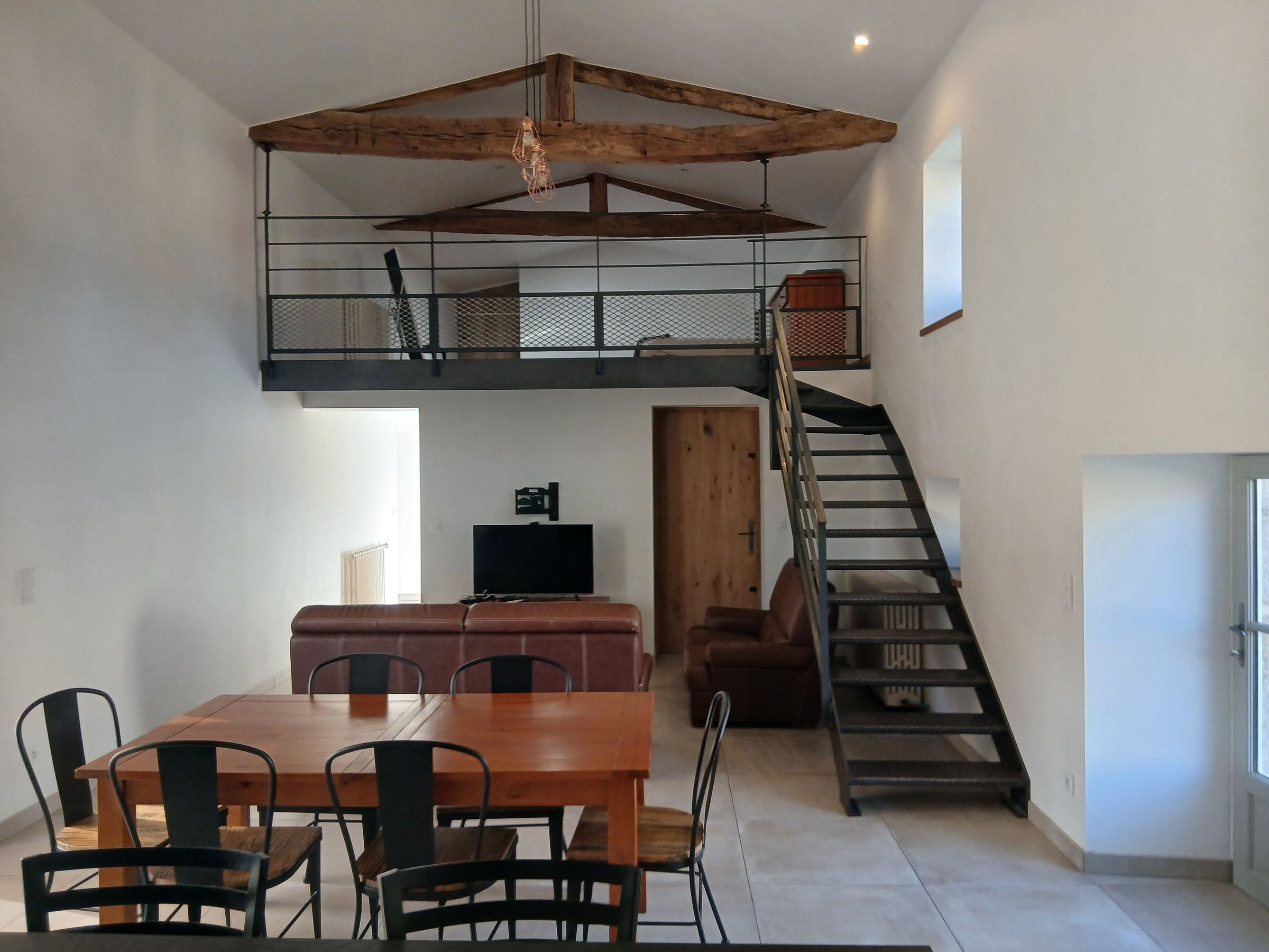 A loft-style room with a dining area, a staircase, and a television.