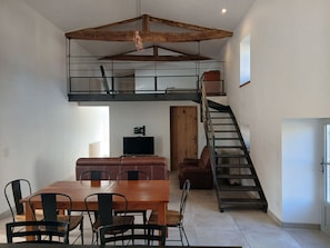 A loft-style room with a dining area, a staircase, and a television. - Countryside cottage near Puy du Fou - 6 guests (Les Herbiers)