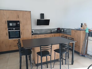 Cocina compacta con armarios de madera, horno integrado, microondas, tostadora y cafetera. Hay una mesa de comedor con cuatro sillas.
