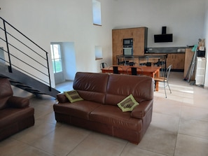 Una sala de estar moderna con un sofá de cuero marrón, un comedor con una mesa y sillas de madera, y una cocina con horno y microondas integrados.