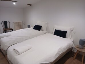Una habitación de hotel con dos camas individuales, una silla, un radiador y una mesita de noche con lámpara.