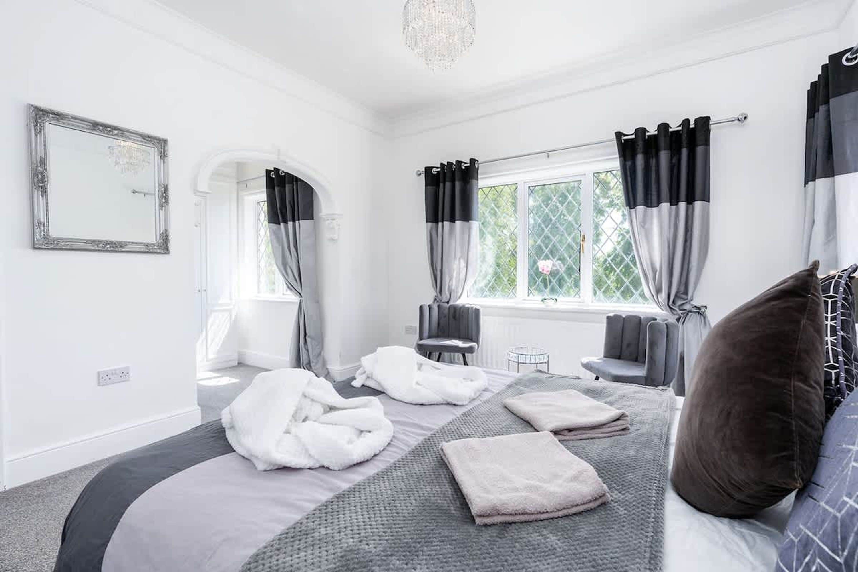 A modern bedroom with a large bed, a sitting area, and a window with curtains.