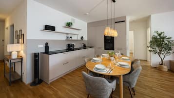 A modern kitchen with a dining area, featuring a wooden table set for six, grey upholstered chairs, a black countertop, and a pendant light.