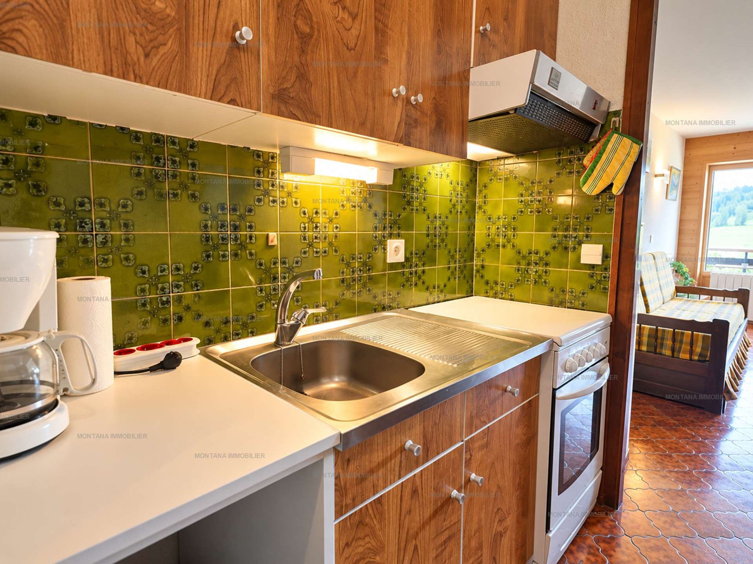 Una cucina con lavello in acciaio inossidabile, mobili in legno e piastrelle verde decorate.