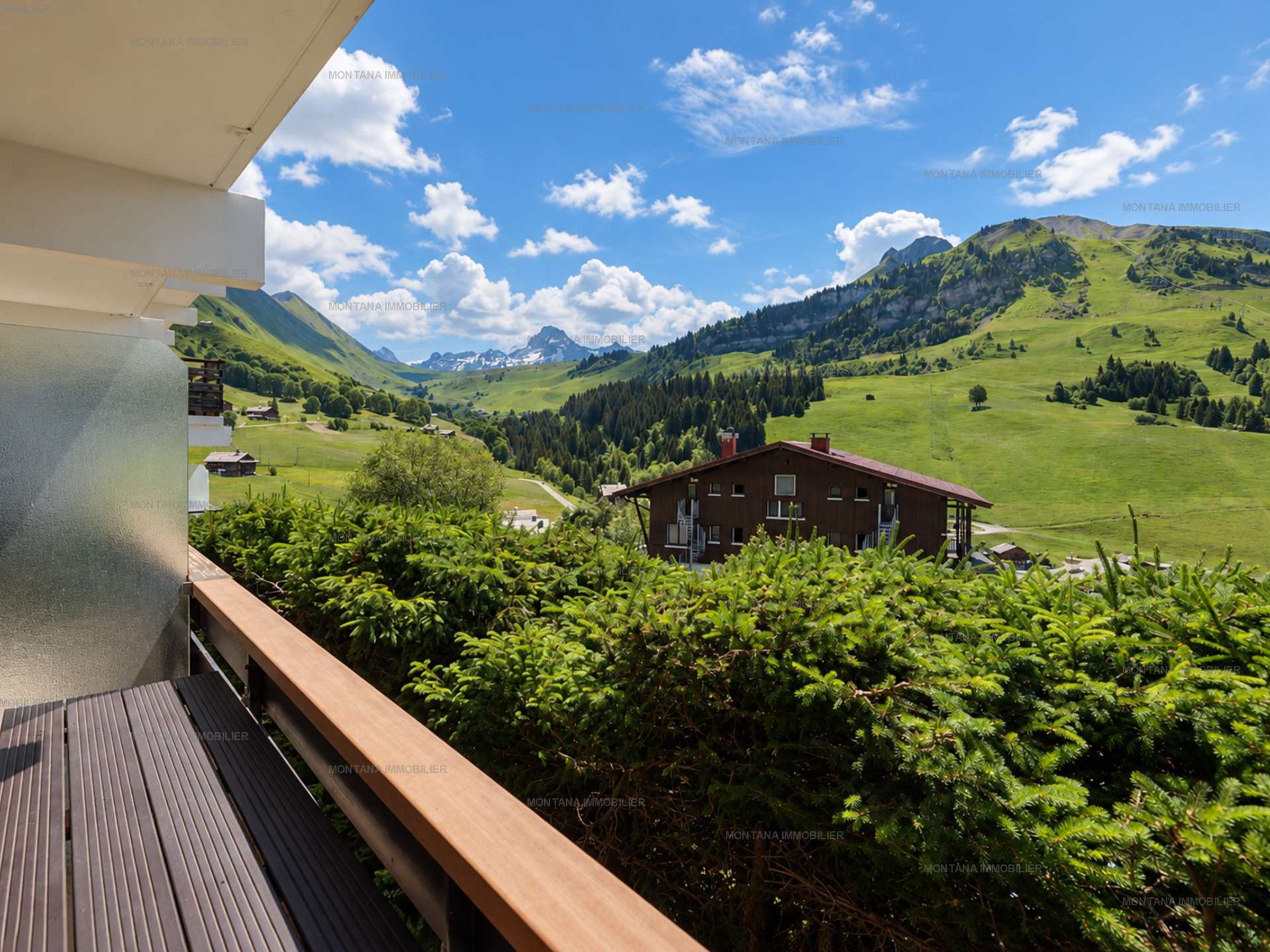 A wooden balcony overlooking a mountainous landscape with a house and greenery.
