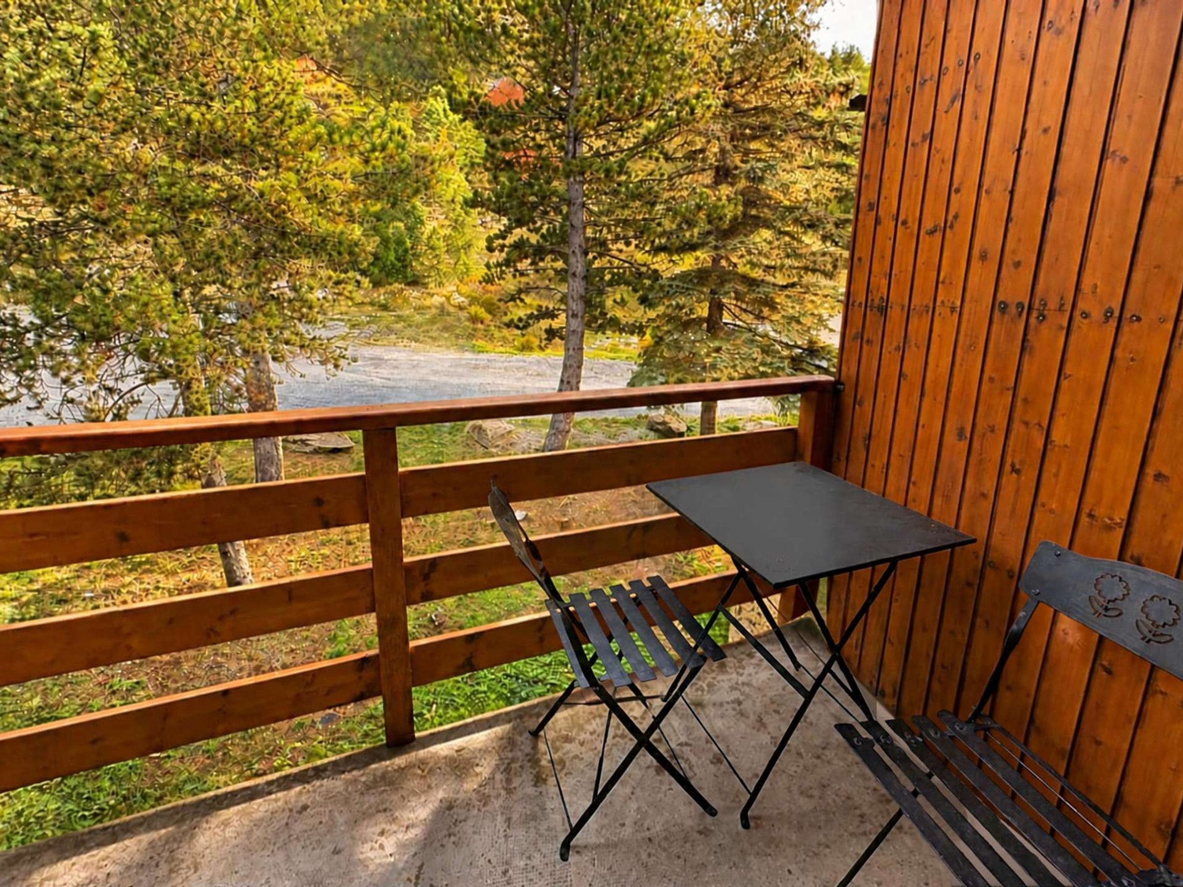 Una terraza de madera con una mesa y un banco, con vistas a un paisaje natural con árboles y una masa de agua.