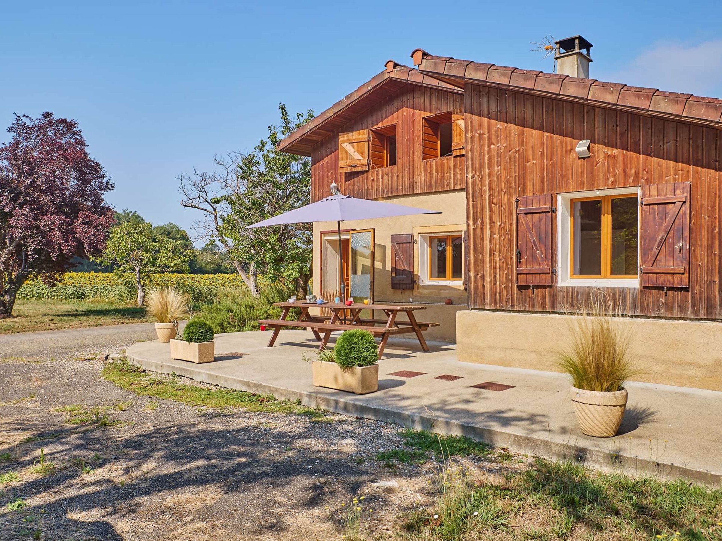 Une maison en bois à deux étages, dotée d’un patio, d’un espace salon extérieur et d’un jardin.