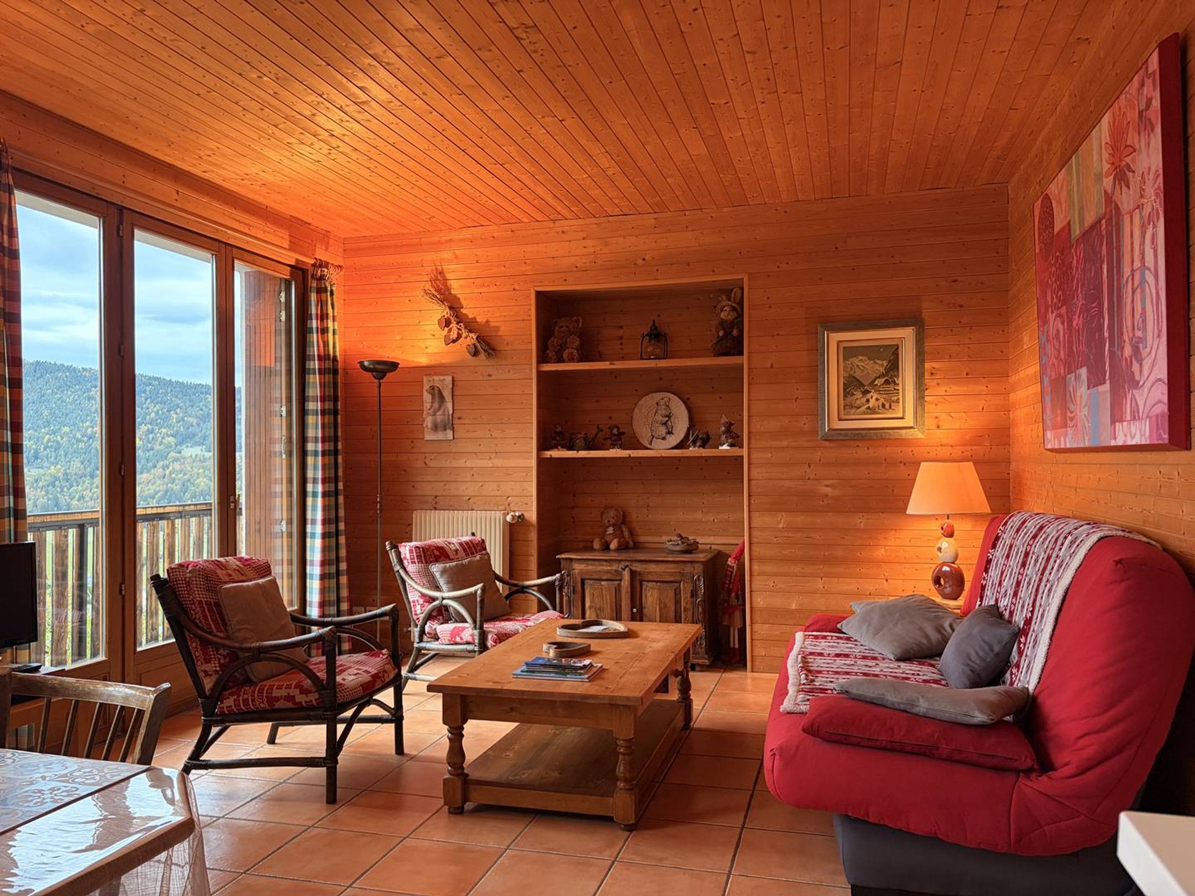 Ein gemütliches Blockhaus-Interieur mit Holzwänden, einer Couch, einem Sessel, einem Tisch und einem Bücherregal.