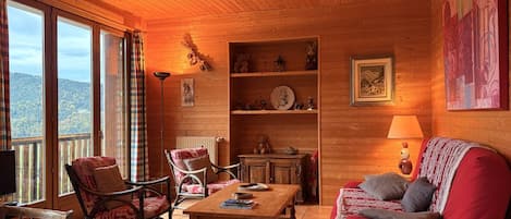 Ein gemütliches Blockhaus-Interieur mit Holzwänden, einer Couch, einem Sessel, einem Tisch und einem Bücherregal.