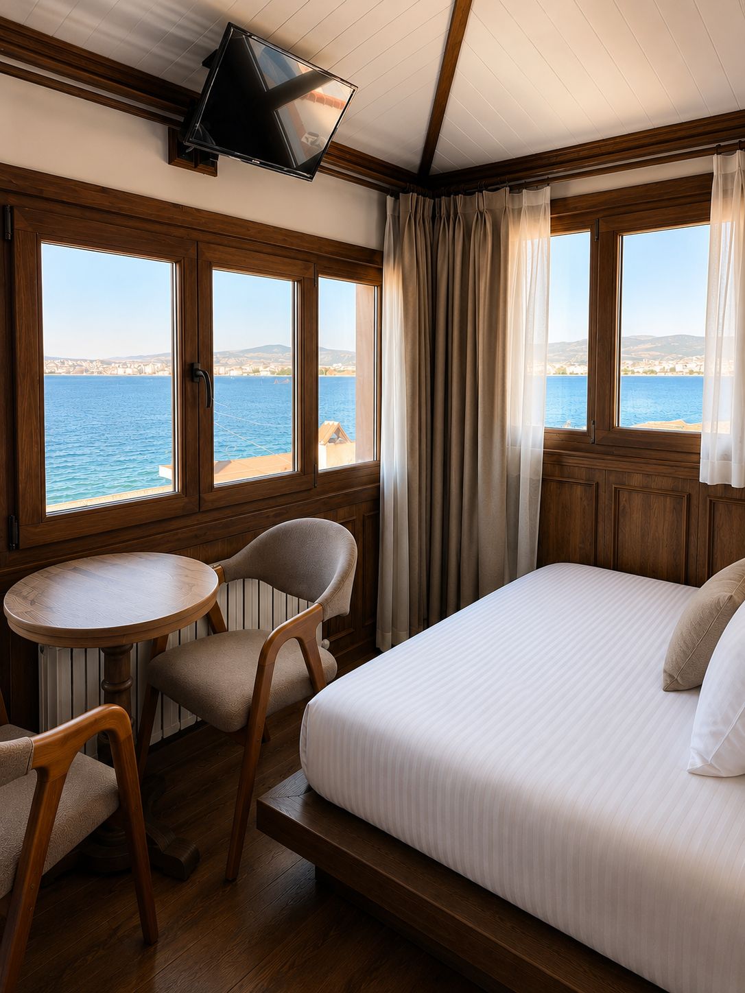 Habitación de hotel con cama, una mesa redonda, dos sillas, televisor y grandes ventanales con vista al mar.