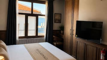 Una habitación de hotel con cama, televisor, ventana con cortinas, una planta y un extintor.