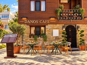 A cafe with outdoor seating, a stone facade, and a signboard.