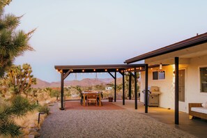 Eine überdachte Terrasse im Freien mit Tisch, Stühlen, einem Grill und Blick auf die Wüstenlandschaft.