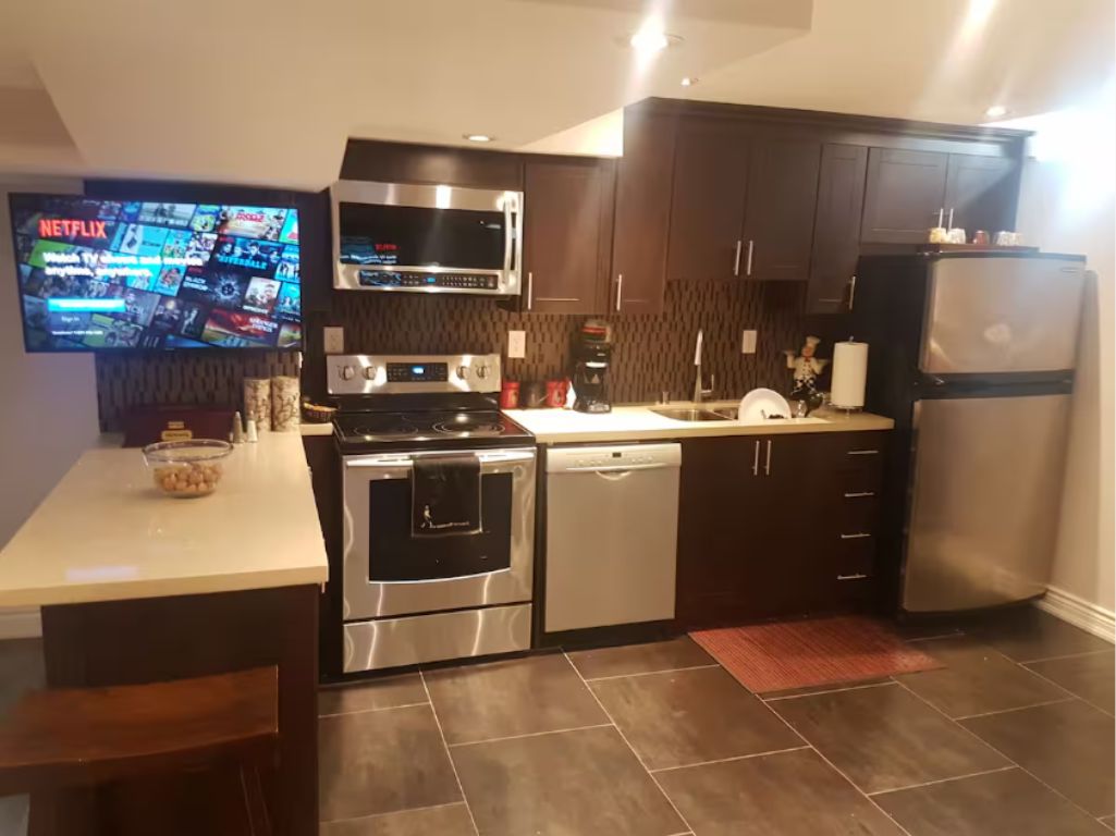 A modern kitchen with a flat-screen TV, stainless steel appliances, and dark cabinetry.