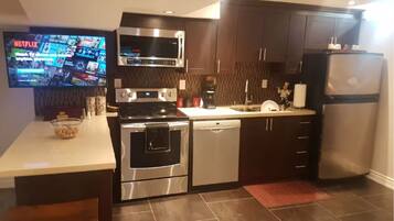A modern kitchen with a flat-screen TV, stainless steel appliances, and dark cabinetry.