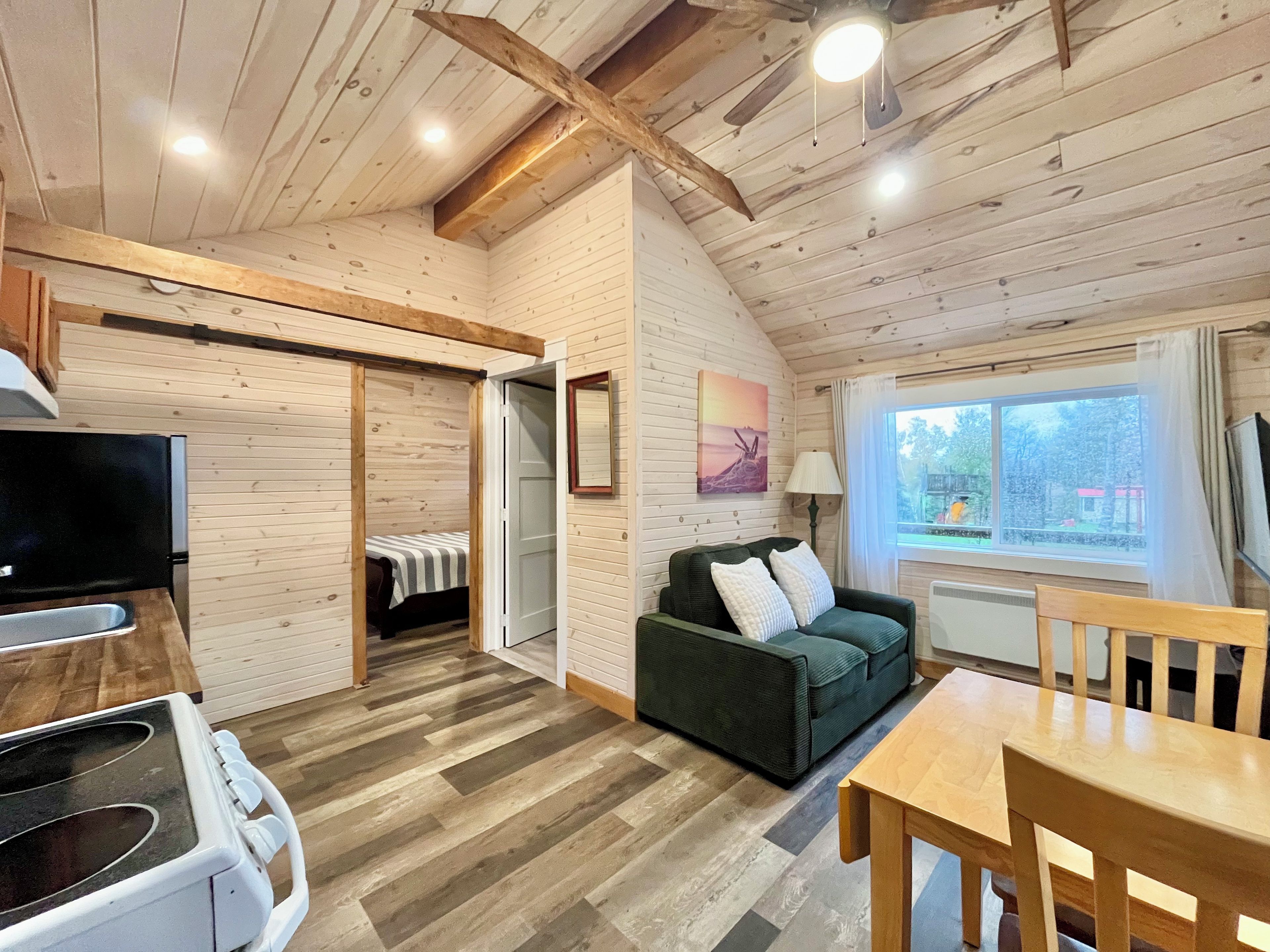 A cozy cabin interior with a dining area, a sofa, a TV, and a window with a view.