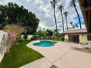A backyard with a swimming pool, a lawn, and a small building with a tiled roof. - Olive Tree Oasis ~ Charming 3B Indian Wells Home (Indian Wells)