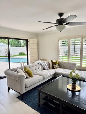 A modern living room with a sectional sofa, a coffee table, and a ceiling fan. - Olive Tree Oasis ~ Charming 3B Indian Wells Home (Indian Wells)