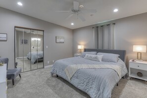 Une chambre à coucher avec un lit, des lampes de chevet, un ventilateur de plafond, un miroir et une porte.