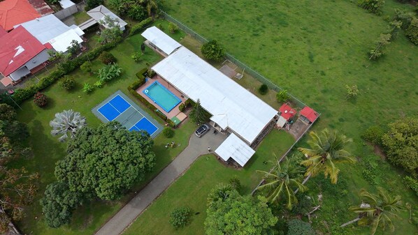 An aerial view of a residential area with a swimming pool, tennis courts, and a large house with a red roof.