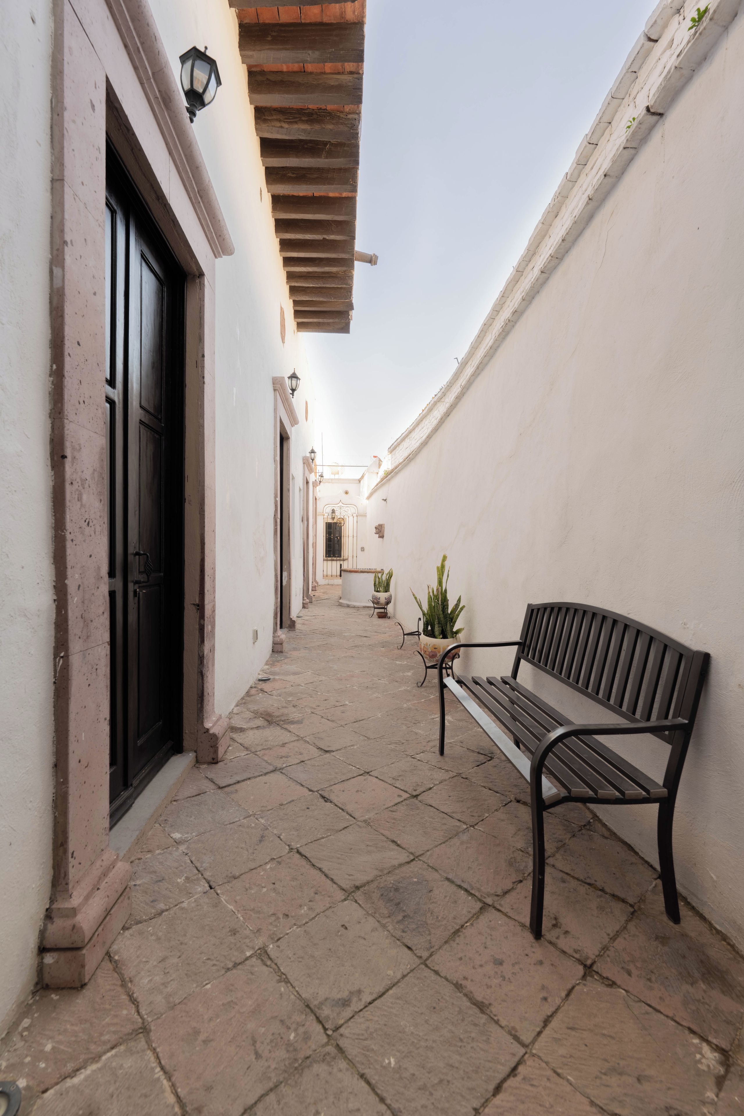 A narrow alleyway with a bench and potted plants.