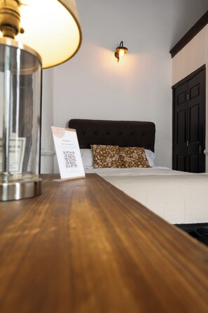 Een hotelkamer met een bed, nachtkastje met lamp, een wandlamp en een deur.