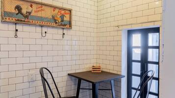 A small dining area with two black chairs, a wooden table, a hanging light fixture, and a wall-mounted picture.