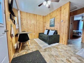 Une pièce aux murs en bois, avec un ventilateur au plafond, un canapé avec des coussins, une petite table et une chaise.