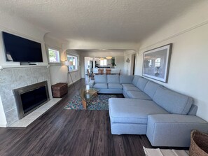 Een moderne woonkamer met een hoekbank, een open haard en een aan de muur bevestigde televisie.