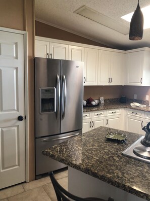 A kitchen with white cabinets, a stainless steel refrigerator, granite countertops, and a hanging light fixture. - Newly renovated 2bedroom mobile home centrally located in Fort Myers@Jamaica Bay (Fort Myers)