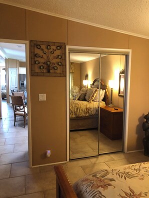A bedroom with a sliding door closet, a bed with floral bedding, a bedside table with a lamp, and a chair in the corner. - Newly renovated 2bedroom mobile home centrally located in Fort Myers@Jamaica Bay (Fort Myers)