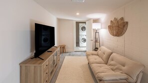 Un salon moderne doté d’un téléviseur à écran plat, d’un meuble en bois, d’un canapé beige et d’un espace buanderie avec un lave-linge.