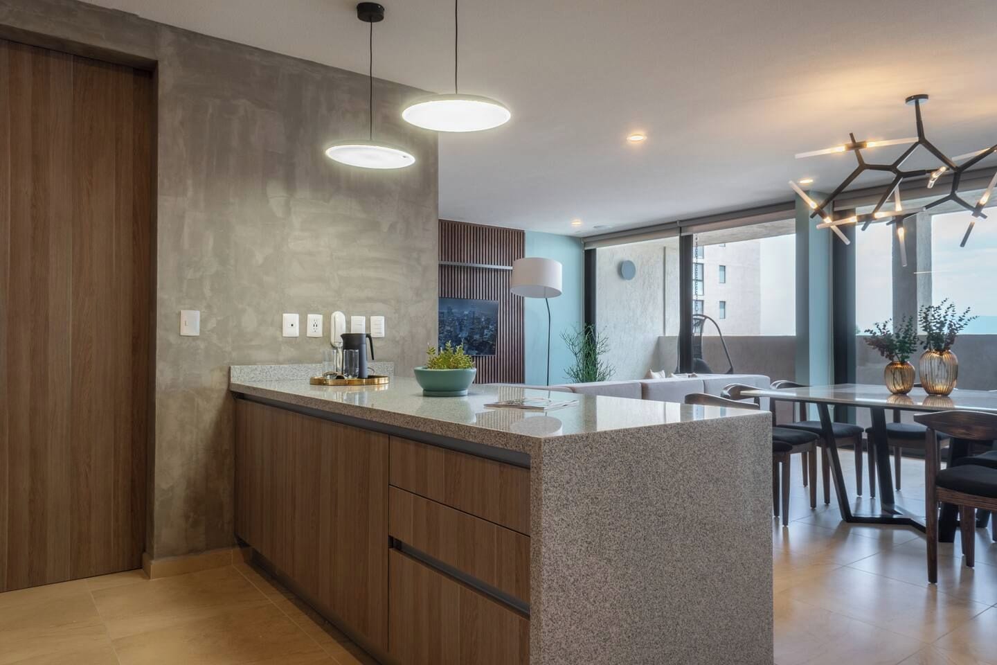 Une cuisine moderne dotée d’un îlot central, de luminaires suspendus et offrant une vue sur l’extérieur.