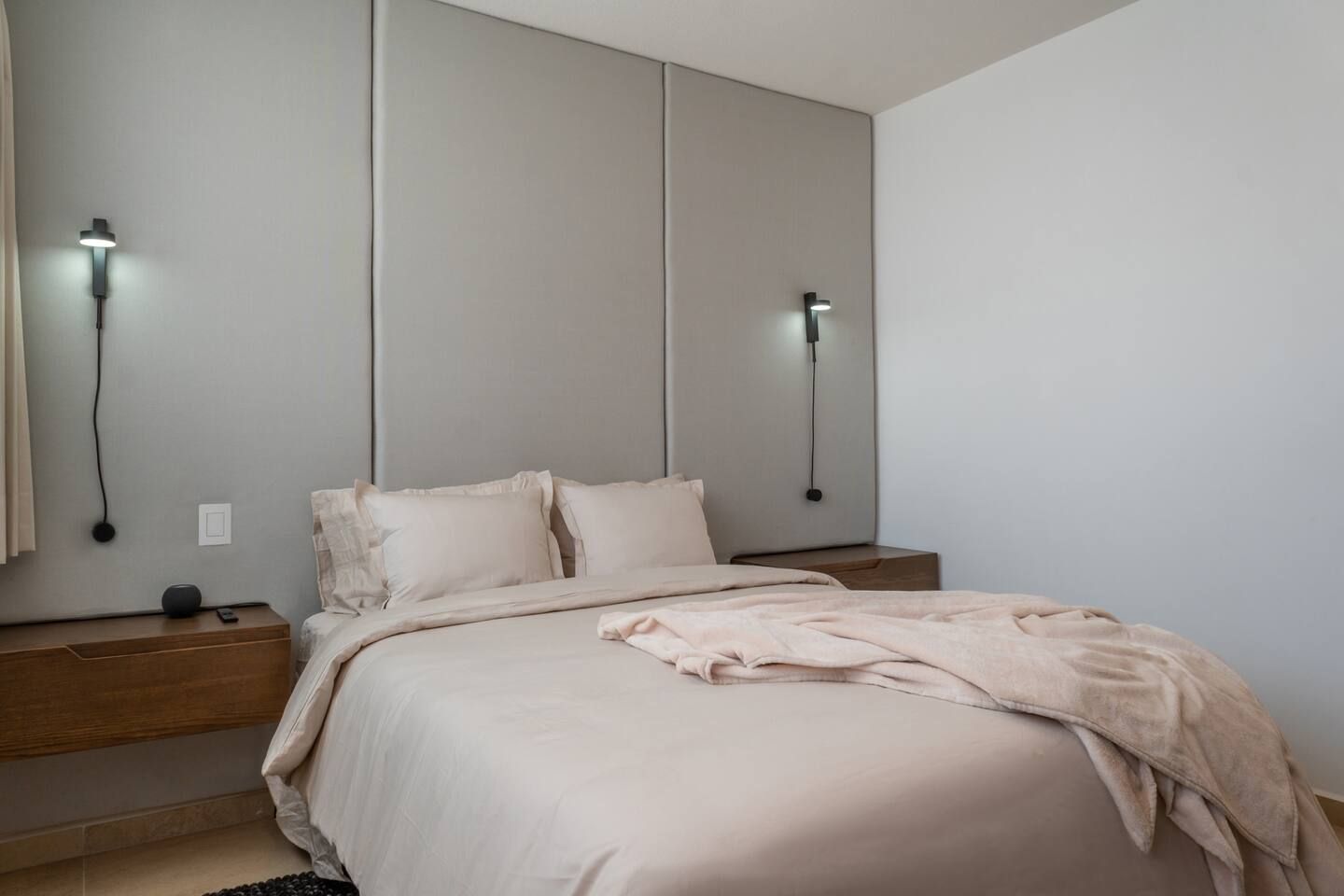 Une chambre à coucher avec un lit, des tables de chevet et des lampes fixées au mur.