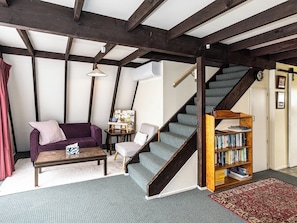 A room with a wooden staircase, a sofa, a chair, a small table, and a bookshelf. - The Mountain Nook -  Ohakune Holiday Home (Ohakune)
