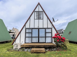 A triangular-roofed building with a wooden deck and a small garden with red flowers. - The Mountain Nook -  Ohakune Holiday Home (Ohakune)