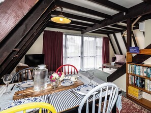 An attic room with a dining table set for two, a bookshelf, and a view of the outside through large windows. - The Mountain Nook -  Ohakune Holiday Home (Ohakune)