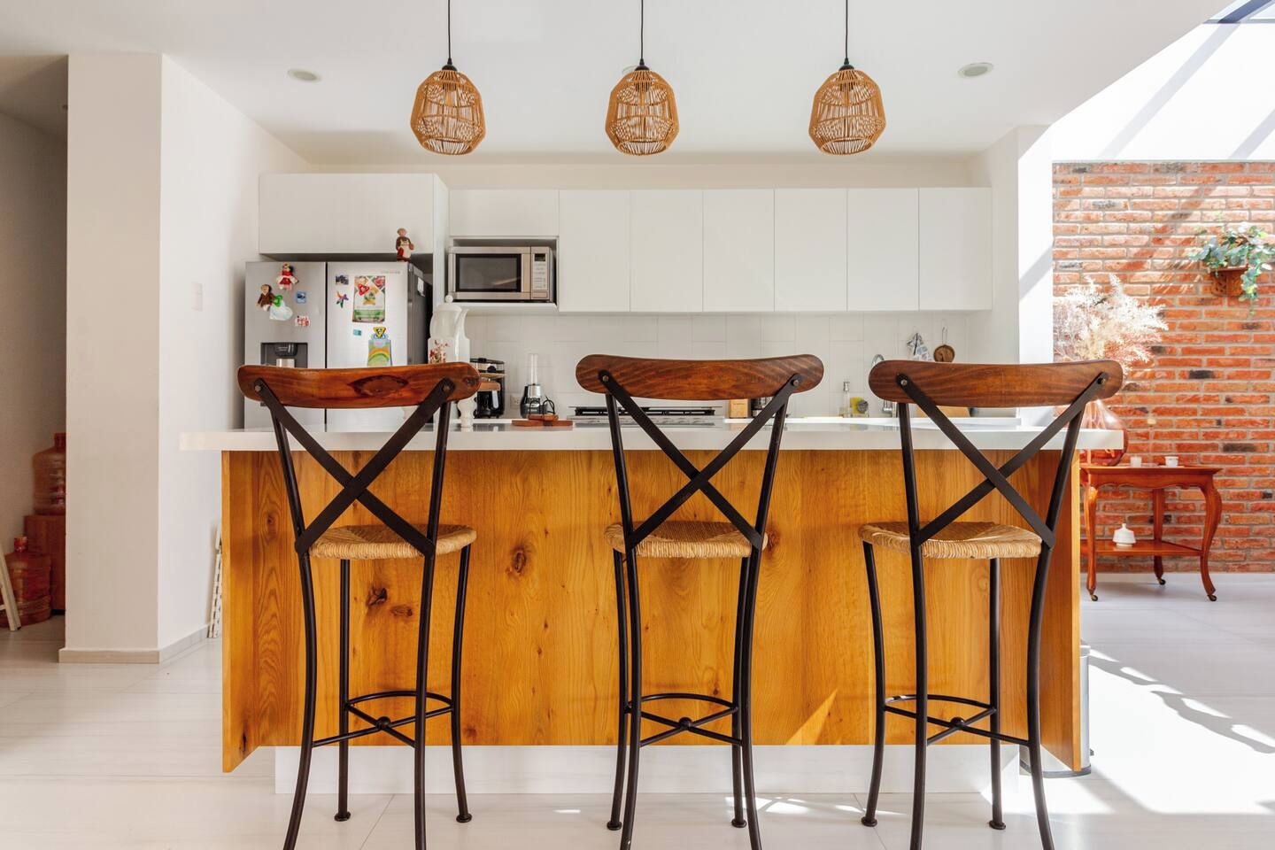 Een moderne keuken met een houten eiland, drie barstoelen en hangende rieten hanglampen.
