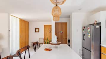 A modern kitchen with a central island, wooden chairs, a refrigerator, and a hanging light fixture.