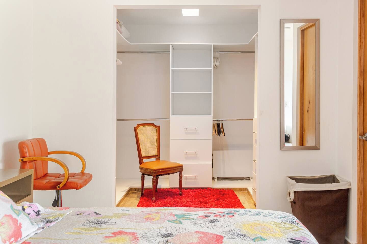 A bedroom with a bed, a chair, a wardrobe, and a red rug.