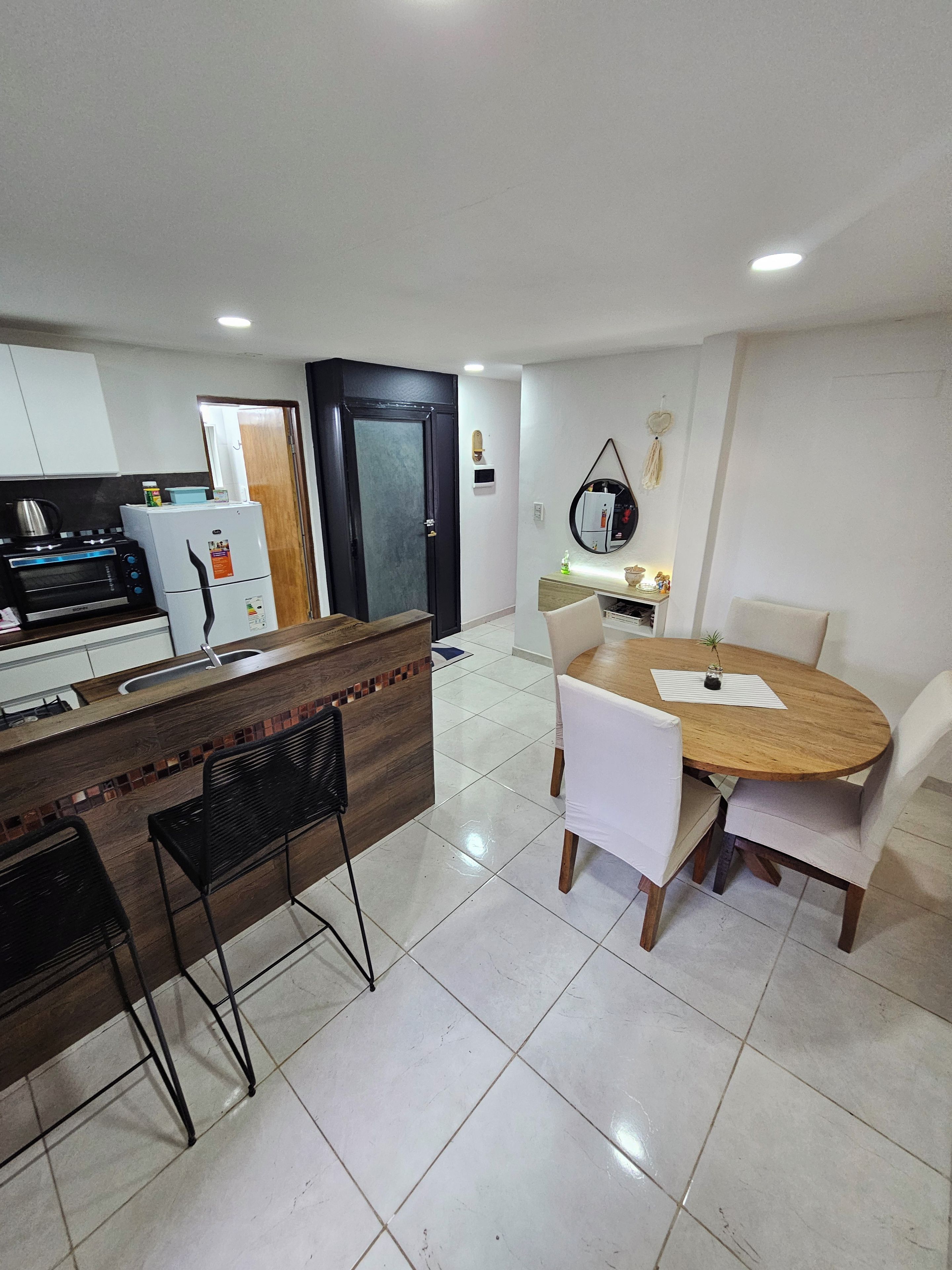 A modern kitchen with a built-in microwave, a refrigerator, and a wooden counter. There is a dining area with a round table and white chairs.