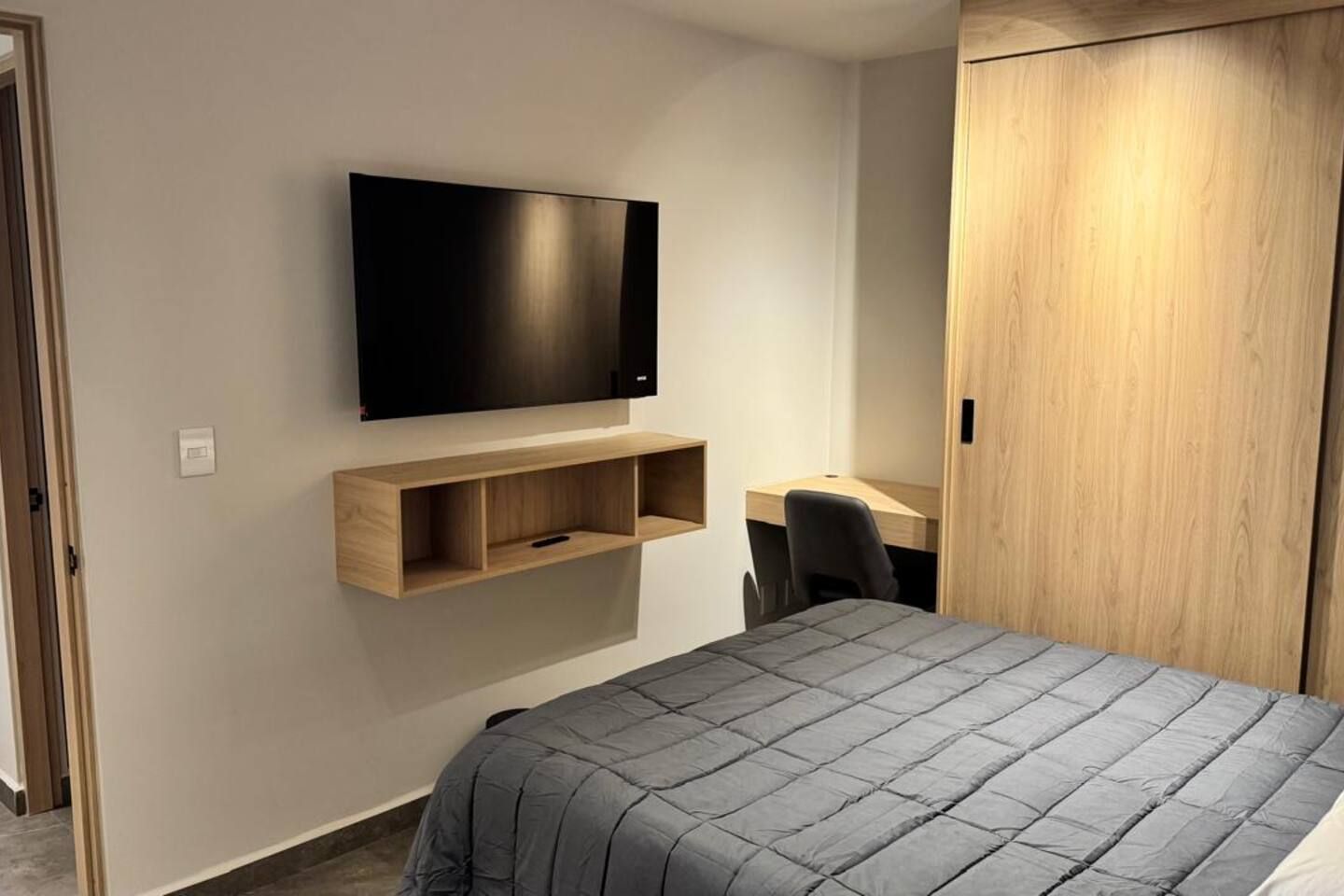 Une chambre à coucher comprenant un lit, un bureau, une chaise et un téléviseur fixé au mur.