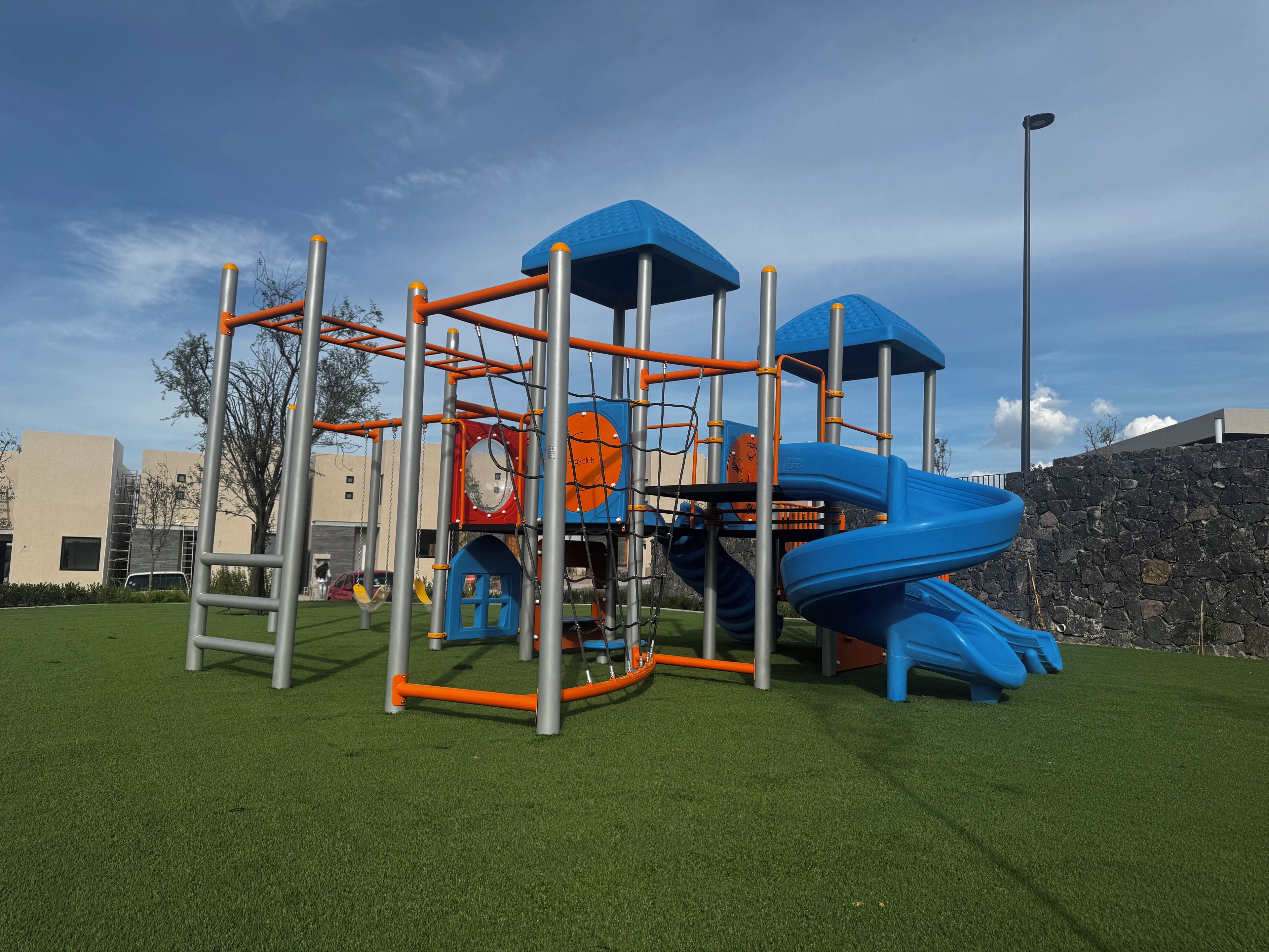 Une aire de jeux avec un toboggan, des structures d’escalade et une zone délimitée par une clôture.