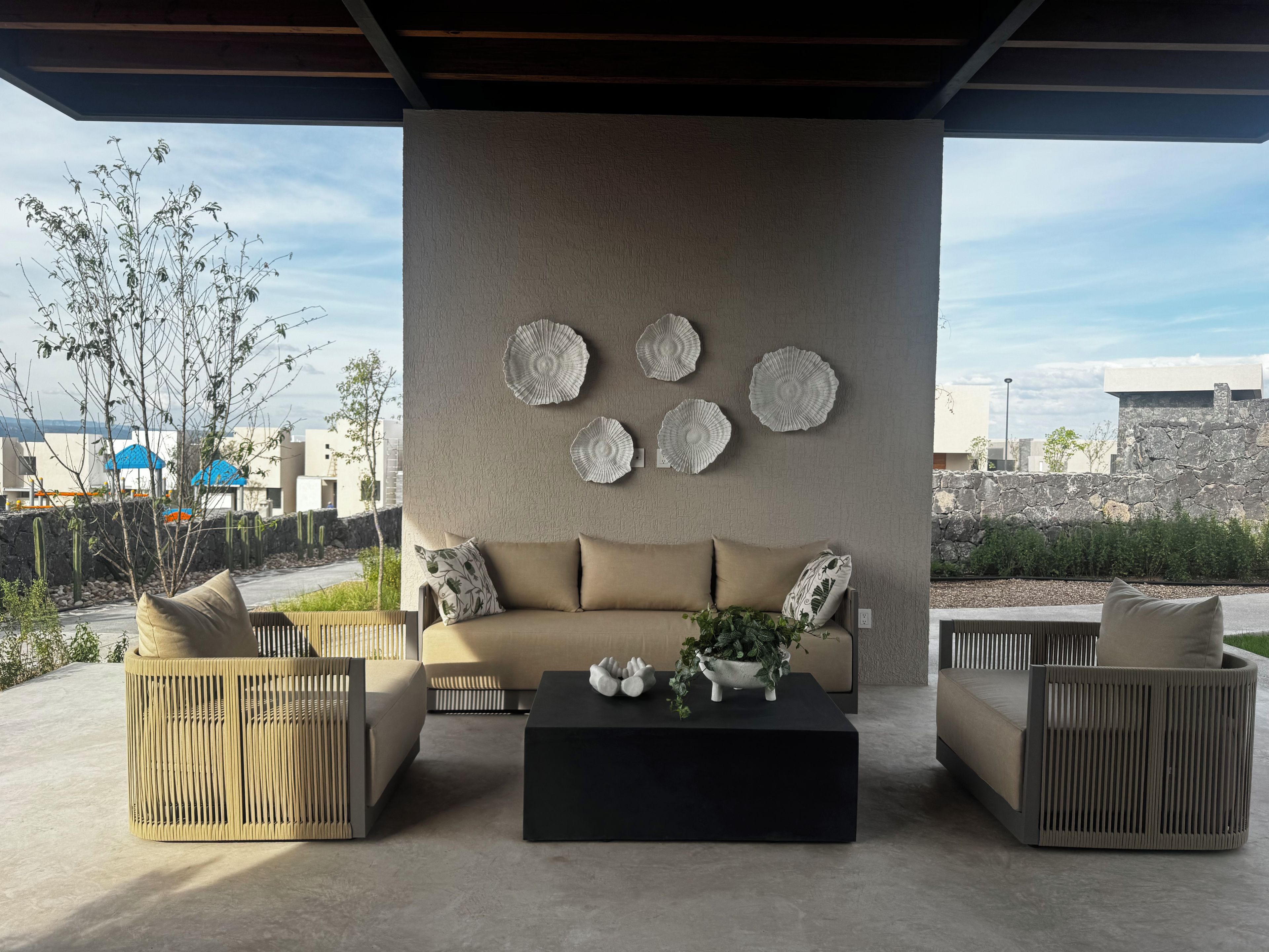 A modern outdoor seating area with a sofa and two chairs, a black coffee table, and decorative wall art.